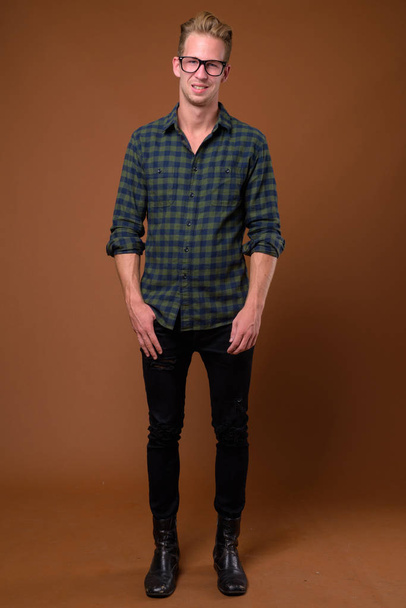 茶色の背景に緑の市松模様のシャツを着ている若いハンサムな男のスタジオ撮影 - 写真・画像