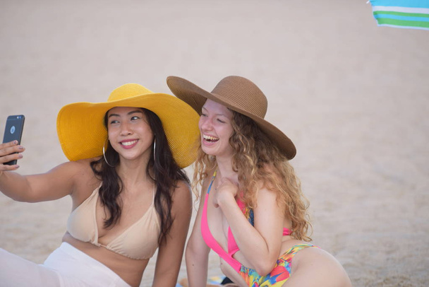Due donne in costume da bagno alla moda appoggiate sulla spiaggia di sabbia
. - Foto, immagini