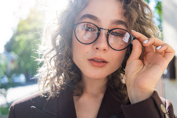 Outdoor close up portrait of young beautiful stylish happy smiling curly girl wearing sunglasses, posing in street. Sunny day light. Summer fashion concept. Copy, empty space for text - Fotoğraf, Görsel