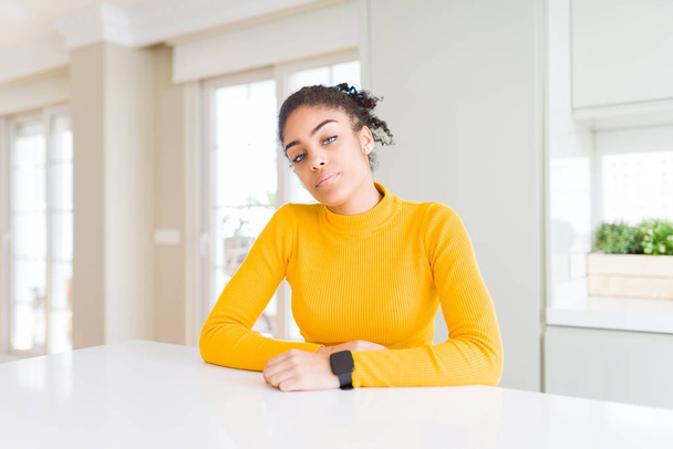 眠くて疲れているように見えるカジュアルな黄色のセーターを着たアフロヘアの美しいアフリカ系アメリカ人女性は、疲労と二日酔いのために疲れ、朝の怠惰な目. - 写真・画像