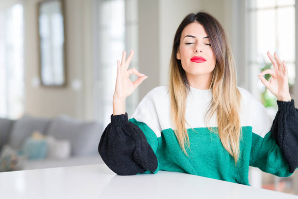若くてきれいな女性の身に着けている冬セーター家庭でリラックスして瞑想の指ジェスチャーをやって閉じた目を浮かべてします。ヨガの概念. - 写真・画像