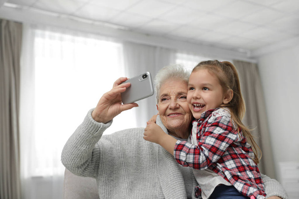 Cute girl and her grandmother taking selfie  at home - Foto, Imagen
