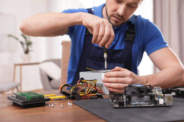 Male technician repairing power supply unit at table indoors - Foto, Imagen