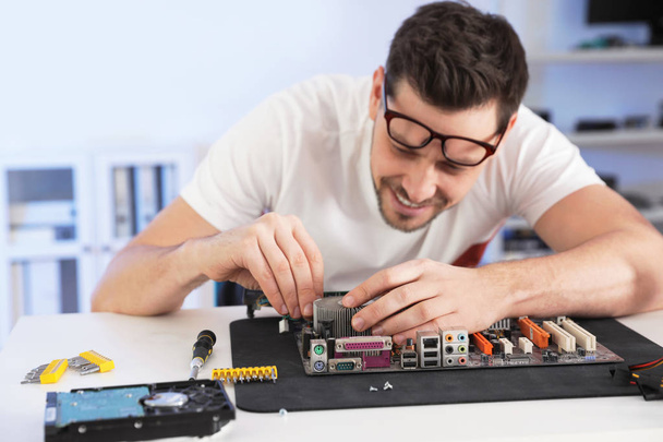 Male technician repairing motherboard at table indoors - 写真・画像