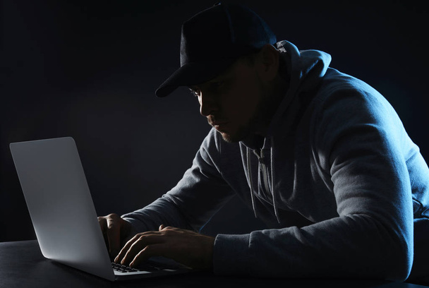 Άνθρωπος που χρησιμοποιεί φορητό υπολογιστή στο τραπέζι σε σκοτεινό φόντο. Εγκληματική δραστηριότητα - Φωτογραφία, εικόνα