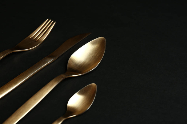Set of gold cutlery on black background. Space for text - Φωτογραφία, εικόνα