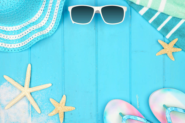 青い木の背景にビーチアクセサリー。コピースペース付きの夏休みコンセプトフレーム。サングラス、貝殻、タオル、フリップフロップ、ストライプハット. - 写真・画像