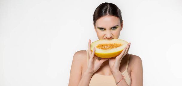 Mode portret van jonge brunette vrouw met groene kunst make-up dat eten meloen met kwade ogen, copyspace voor uw tekst gesneden - Foto, afbeelding