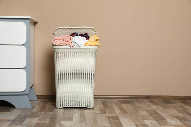 Cesta de lavandaria de plástico com roupas sujas perto da parede de cor no quarto. Espaço para texto
 - Foto, Imagem