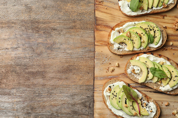 Board with avocado bruschettas on wooden table, flat lay. Space for text - Fotoğraf, Görsel