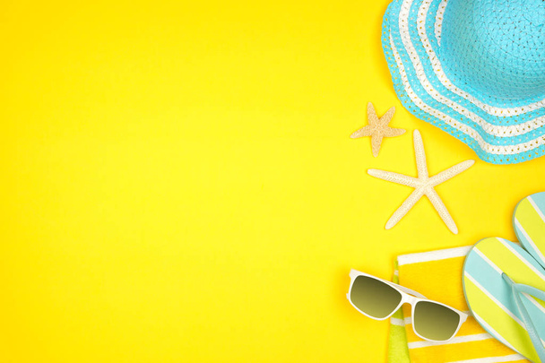 黄色の背景にビーチアクセサリー。夏休みコンセプトサイドボーダーとコピースペース。サングラス、貝殻、タオル、フリップフロップ、青い縞模様の帽子. - 写真・画像