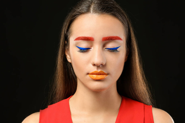 Young woman with dyed eyebrows and creative makeup on black background - Photo, Image