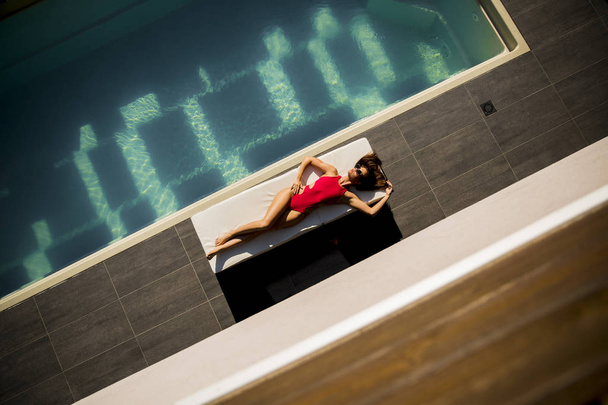 З видом на красиву засмаглу жінку з сонцезахисними окулярами в червоному бікіні, що розслабляється біля розкішного басейну
 - Фото, зображення