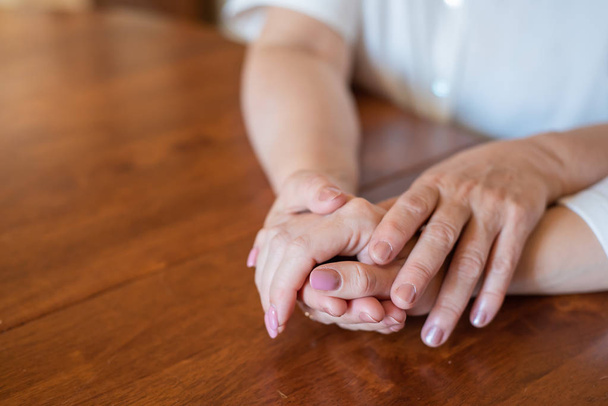 Elderly mother and her daughter holding hands while sitting at the table.Close up on women of different generations holding hands. Close Up Shot Of Mother And Daughter's Hands Holding - Foto, imagen