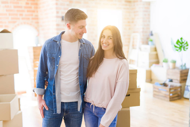 schönes junges Paar, das sich verliebt umarmt und die Tafel hält, die in ein neues Zuhause umzieht, glücklich lächelnd für eine neue Wohnung - Foto, Bild