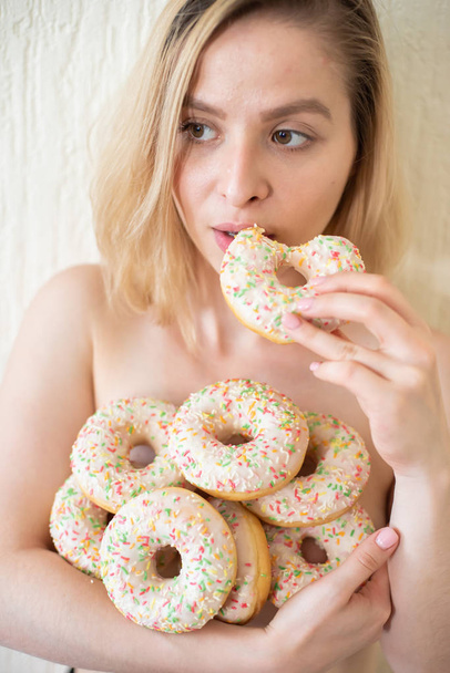 Nude young woman eating donuts. Portrait of an attractive woman with a mountain of donuts - 写真・画像