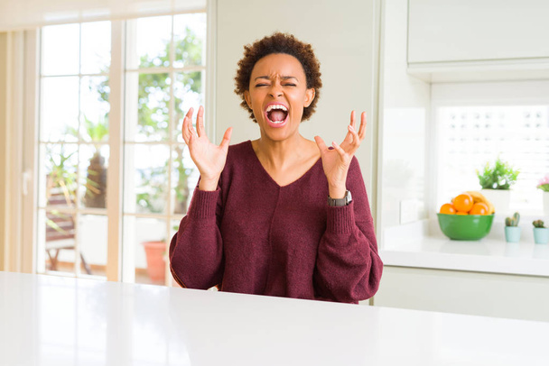Young beautiful african american woman at home crazy and mad shouting and yelling with aggressive expression and arms raised. Frustration concept. - Foto, Bild