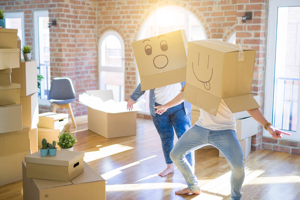 Crazy couple wearing cardboard boxes with funny emoji faces over head, having fun at new house - Photo, Image