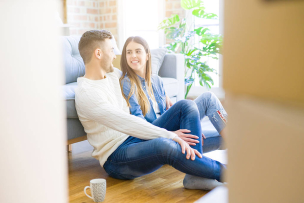 Joven hermosa pareja sentada en el piso del nuevo apartamento, sonriendo en el amor feliz por mudarse a un nuevo hogar
 - Foto, imagen