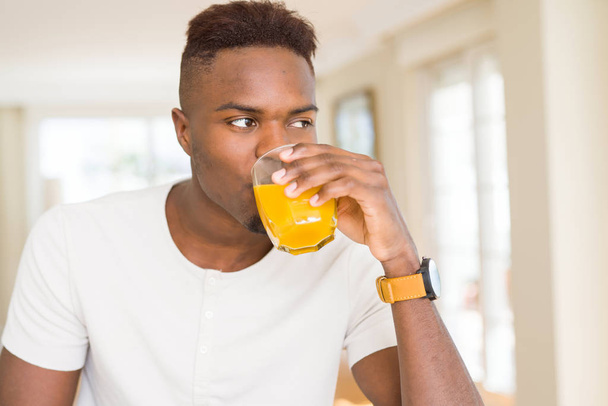 Красивий молодий африканський чоловік п'є склянку свіжого натурального апельсинового соку, насолоджуючись фруктовим освіжаючим
 - Фото, зображення
