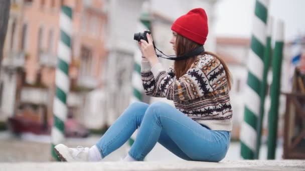 Młoda loughing kobieta siedzi na betonowych blokach w pobliżu rzeki i robi zdjęcia - Materiał filmowy, wideo