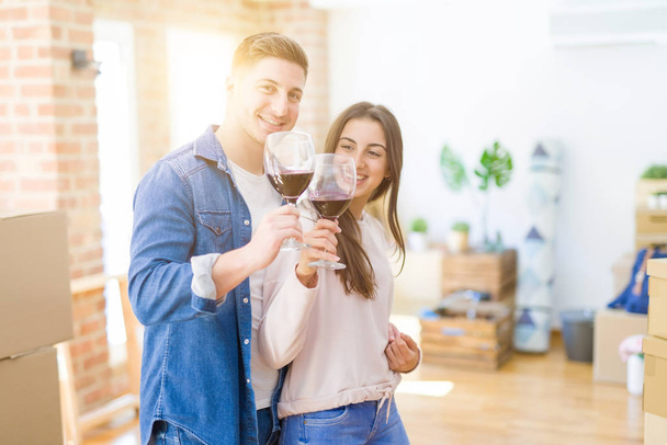 Young beautiful couple drinking a glass of wine celebrating moving to a new house - Photo, Image