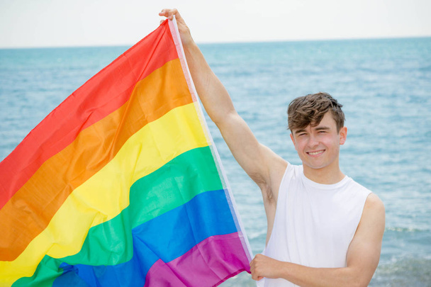Caucasian male on a beach holding a Pride flag - Photo, Image