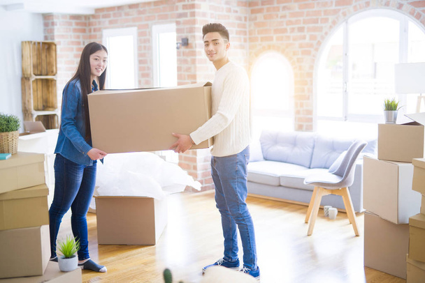 Beautiful young asian couple looking happy, holding a big cardboard box smiling excited moving to a new home - Foto, imagen
