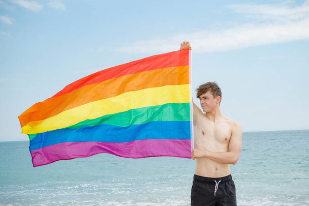 Caucasian male on a beach holding a Pride flag - Фото, изображение