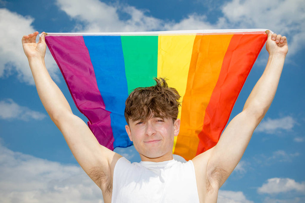 Caucasian male on a beach holding a Pride flag - Photo, image
