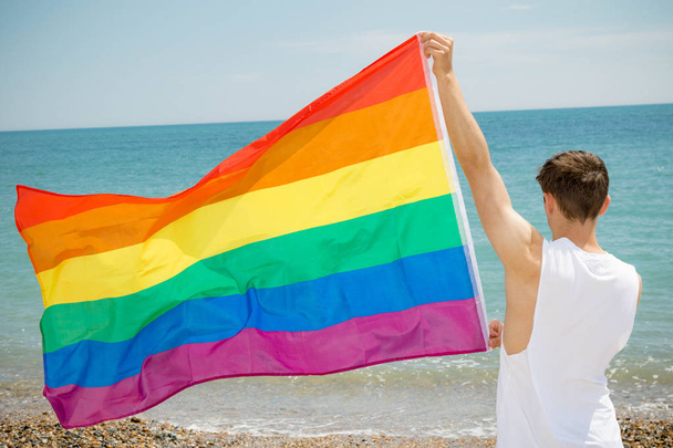 Hombre caucásico en una playa con bandera de Orgullo
 - Foto, imagen