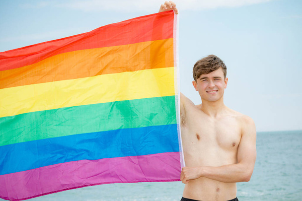 Caucasian male on a beach holding a Pride flag - Foto, Imagem