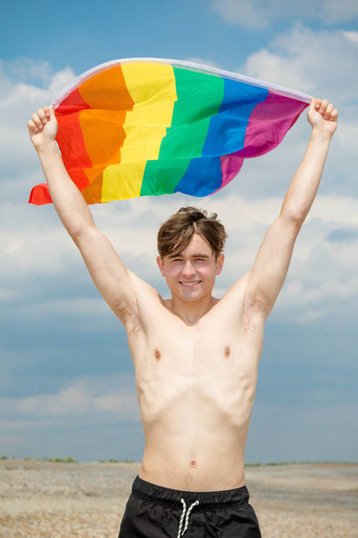 Caucasian male on a beach holding a Pride flag - Fotoğraf, Görsel