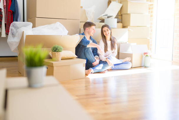 Молода красива пара розслабляється сидячи на підлозі навколо картонних коробок вдома, посміхаючись щасливо переїжджаючи в новий будинок
 - Фото, зображення