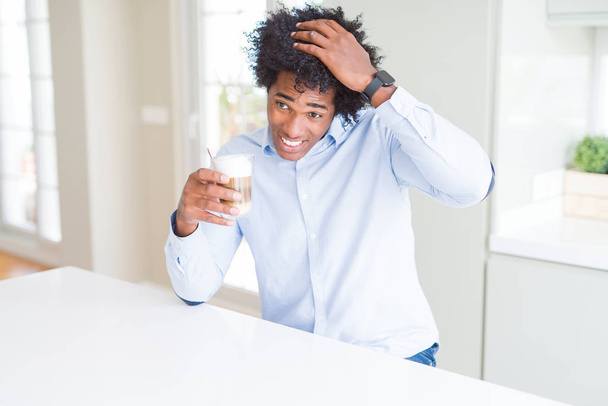African American man met Afro haar drinken van een kopje koffie gestrest met de hand op het hoofd, geschokt met schaamte en verrassing gezicht, boos en gefrustreerd. Angst en boos voor fout. - Foto, afbeelding