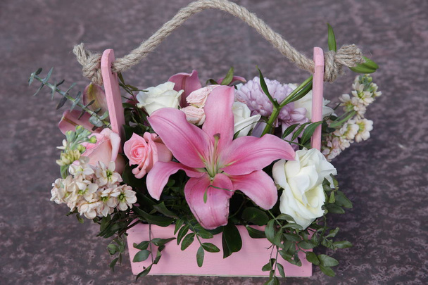 buquê de flores rosa e branco em uma cesta de madeira com uma alça de fibra natural em um fundo rosa cinza
 - Foto, Imagem