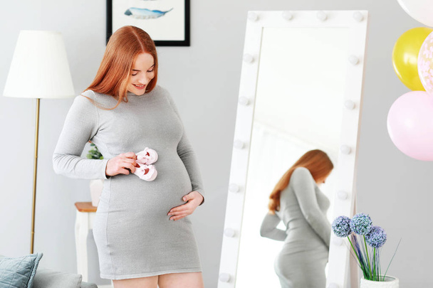 Beautiful pregnant woman with baby booties at home - 写真・画像