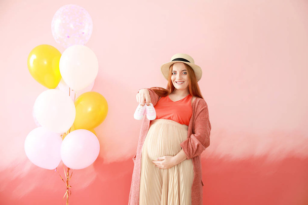 Beautiful pregnant woman with baby booties and air balloons on color background - Foto, Bild
