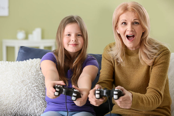 Mature woman and her cute granddaughter playing video game at home - Фото, изображение