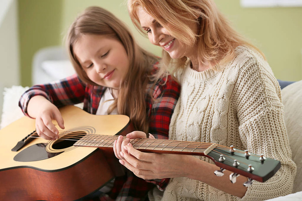 Little girl playing guitar for her grandmother at home - Foto, Imagen