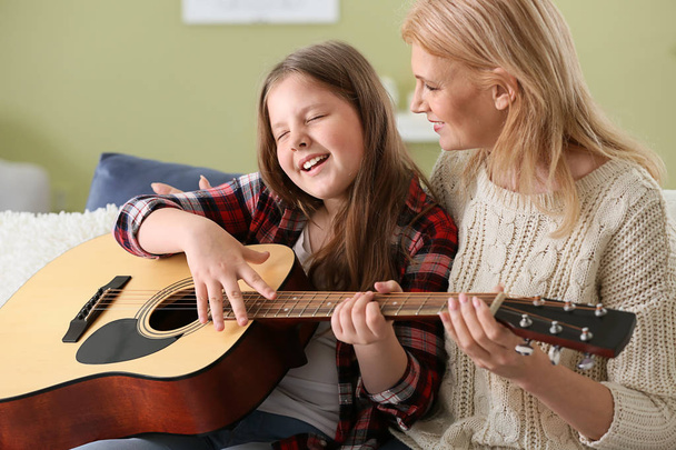 Little girl playing guitar for her grandmother at home - Фото, изображение