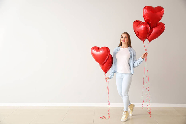 Beautiful young woman with heart-shaped air balloons near light wall - 写真・画像