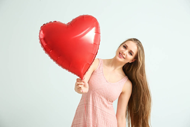 Beautiful young woman with heart-shaped air balloon on light background - Φωτογραφία, εικόνα