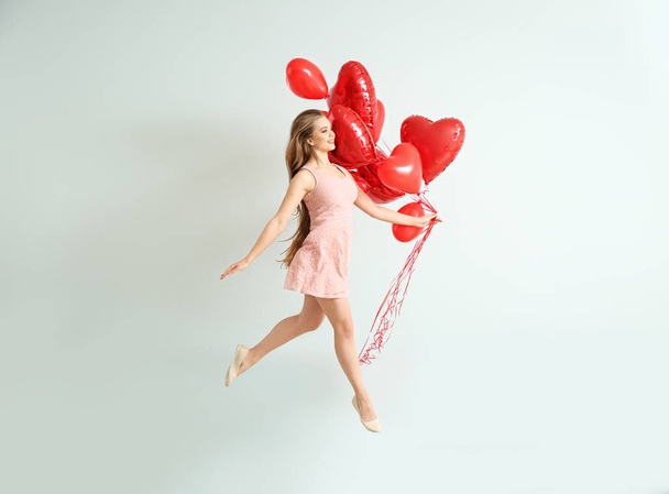 Bella giovane donna spensierata con palloncini d'aria a forma di cuore vicino alla parete luminosa
 - Foto, immagini