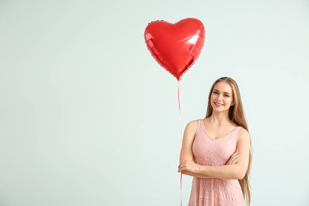 Beautiful young woman with heart-shaped air balloon on light background - Foto, imagen