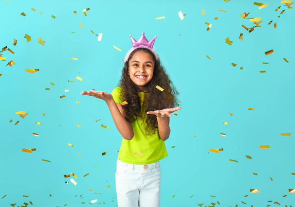 Cute African-American girl with crown and falling confetti on color background - Zdjęcie, obraz