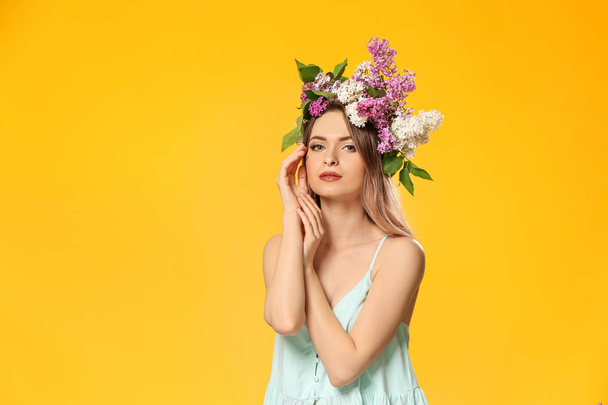 Mooie jonge vrouw met lila bloemen op haar hoofd tegen kleur achtergrond - Foto, afbeelding
