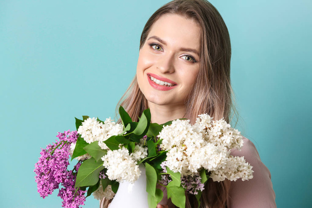 Beautiful young woman with bouquet of lilac flowers on color background - Foto, Imagem
