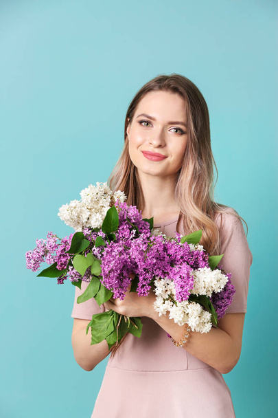 Beautiful young woman with bouquet of lilac flowers on color background - Photo, Image