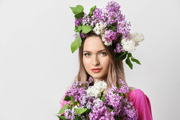 Mooie jonge vrouw met lila bloemen op lichte achtergrond - Foto, afbeelding